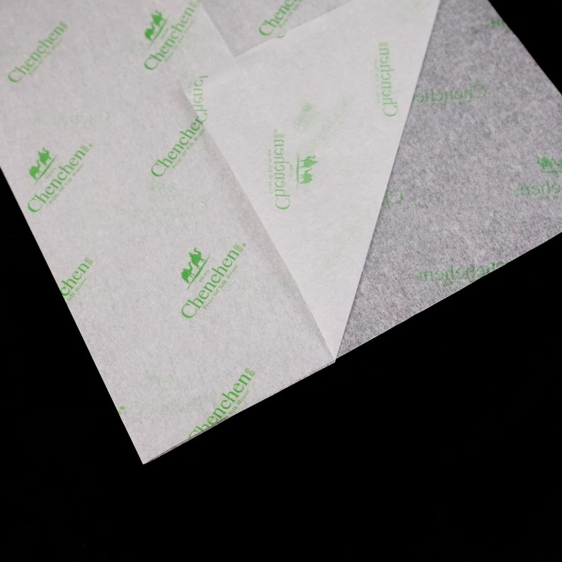 May include: Close-up of two sheets of white tissue paper with a green logo that says "Chenchen, Trust of Quality Life" printed on them. The tissue paper is folded in half and the edges are visible.