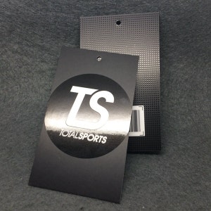 Pode incluir: Etiqueta de pendurar preta e prateada com um c&iacute;rculo branco contendo as letras "TS" e o texto "TOTALSPORTS".