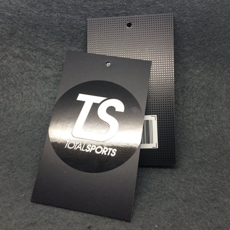 Pode incluir: Etiqueta de pendurar preta e prateada com um c&iacute;rculo branco contendo as letras "TS" e o texto "TOTALSPORTS".