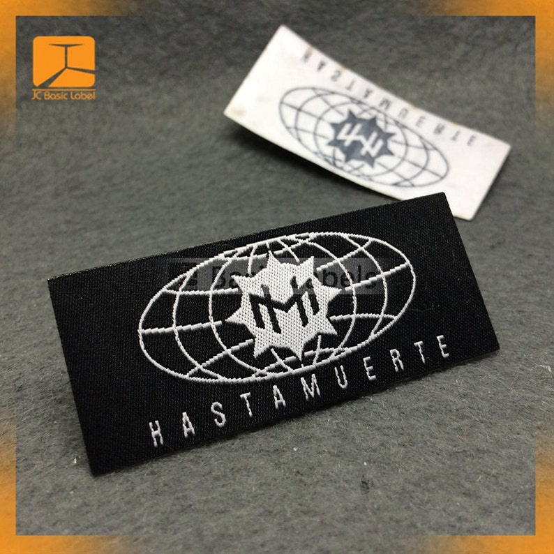 May include: Black woven label with white text and a logo. The logo is a stylized globe with a star in the center. The text reads "HASTA MUERTE" and "HM".