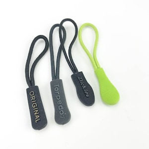 May include: Three zipper pulls with different brand names. The zipper pulls are black with gold lettering and a green zipper pull. The brands are "Original", "Torpedo7", and "Dickies".