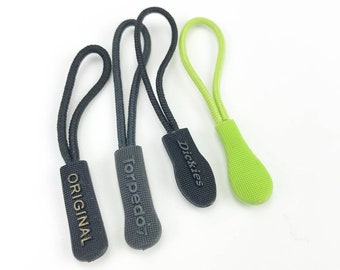Könnte beinhalten: Drei Reißverschluss-Zipper mit verschiedenen Markennamen. Die Reißverschluss-Zipper sind schwarz mit goldener Beschriftung und ein grüner Reißverschluss-Zipper. Die Marken sind "Original", "Torpedo7" und "Dickies".