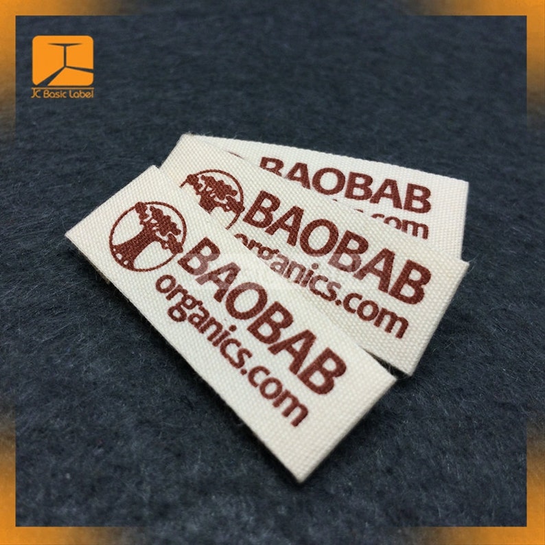 Pode incluir: Tr&ecirc;s etiquetas retangulares de tecido com o texto "BAOBAB organics.com" em castanho. As etiquetas s&atilde;o branco-sujo com um log&oacute;tipo de &aacute;rvore castanha. As etiquetas est&atilde;o empilhadas umas sobre as outras.