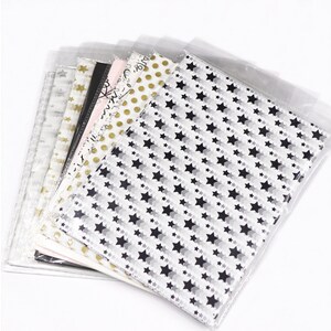 May include: A stack of tissue paper in various patterns, including stars, polka dots, and abstract designs. The tissue paper is packaged in clear plastic bags.