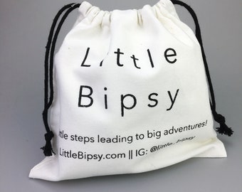 May include: White cotton drawstring bag with black drawstrings. The bag has black text that reads "Little Bipsy" and "little steps leading to big adventures! LittleBipsy.com || IG: @little_bipsy"