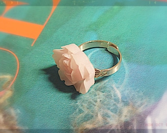 May include: A delicate ring featuring a white rose-shaped design. The ring is made of silver and has a simple band.