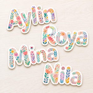 Può includere: Quattro adesivi con nomi personalizzati che riportano Aylin, Roya, Mina e Nila. Ogni lettera è riempita con un colorato motivo floreale ad acquerello con elementi botanici rosa, blu, gialli e verdi e un bordo bianco fustellato.