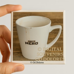 Könnte beinhalten: Weiße Kaffeetasse aus Keramik mit dem Text "CAFFE NERO" in Schwarz. Die Tasse hat einen Henkel und scheint Kaffeeflecken im Inneren zu haben. Das Bild befindet sich auf einer quadratischen Fliese mit dem Text "DIGITAL SOUVENIRS OD DOLORES".