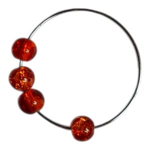 May include: A silver-toned metal bracelet with four round, orange-red beads. The beads have a textured, crackled appearance, and are evenly spaced along the bracelet's curved design. The bracelet is set against a white background.