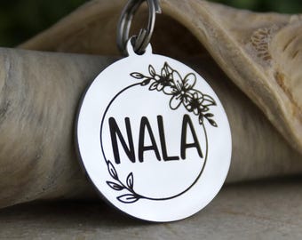 May include: Silver pet tag with a floral design and the name "NALA" engraved in black.