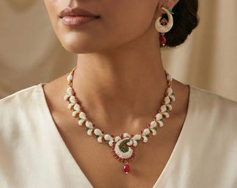 May include: A gold-toned necklace and matching earrings set. The necklace features a floral design with white, green, and red accents. A teardrop-shaped red gem hangs from the center. The earrings have a similar design.