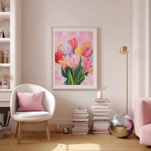 floral art print featuring a bouquet of colorful tulips in shades of pink, red, yellow, and blue. The artwork is displayed in a light-filled room with a white chair, pink pillow, and a pink sofa. A disco ball and stacks of books add decorative elements.