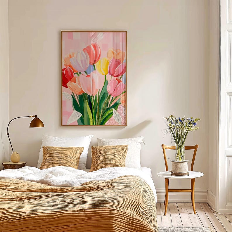 The artwork depicts a bouquet of colorful tulips in shades of pink, red, yellow, and white. The painting hangs above a bed with white pillows and a mustard-colored blanket. A small side table with a vase of flowers sits nearby.