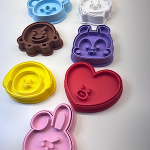 Op de afbeelding: Een verzameling kleurrijke koekjessnijders in verschillende vormen, waaronder een beer, een leeuw, een chipmunk, een hart, een bloem en een konijn. De snijders zijn in blauw, wit, bruin, paars, geel, rood en roze.