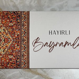 Könnte beinhalten: Rechteckige Karte mit einem Muster auf der linken Seite, das Rot-, Orange- und Beigetöne kombiniert. Die rechte Seite ist weiß mit dem Schriftzug "HAYIRLI Bayramlar" in brauner Schrift.