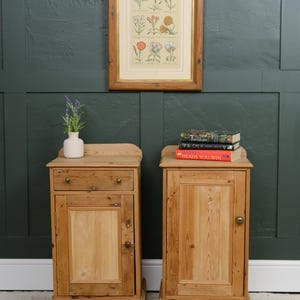 May include: A pair of light brown wooden bedside cabinets with a natural grain finish. The left cabinet features a single drawer and a door with a round knob. The right cabinet has a single door with a round knob. Both have a raised back edge.