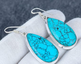 May include: A pair of turquoise teardrop earrings. Each earring features a vibrant blue-green stone with dark veining, set in a silver-colored metal frame. The earrings have a simple hook design for pierced ears, showcasing a classic jewelry style.