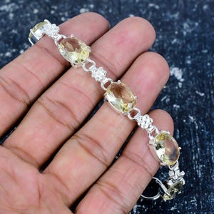 Pode incluir: Uma pulseira de prata com pedras preciosas ovais amarelo claro. A pulseira tem detalhes florais entre as pedras preciosas. As pedras são engastadas em prata. A pulseira é exibida em um fundo escuro.