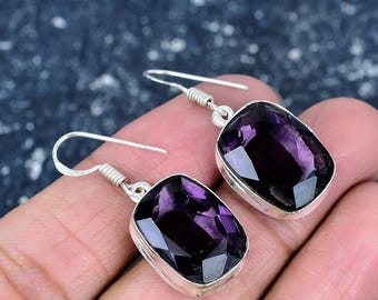 May include: A pair of silver earrings featuring large, rectangular, faceted amethyst gemstones. The deep purple stones are set in a silver bezel and have a polished, reflective surface. The earrings are designed for pierced ears.