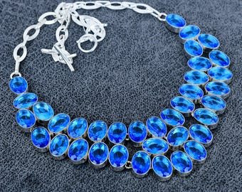 May include: A silver necklace featuring oval-cut, bright blue gemstones. The gemstones are set in a silver metal and arranged in a double-strand design. The necklace has a toggle clasp and a chain-link extension.
