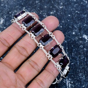 May include: A silver bracelet featuring rectangular, deep purple gemstones. The bracelet has a chain-like design with the gemstones set in individual silver frames. The gemstones are a rich, dark color, and the silver has a polished finish.
