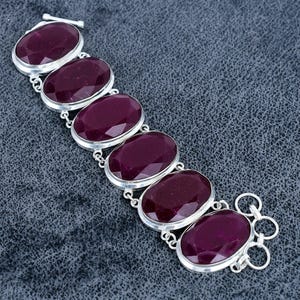 May include: A silver bracelet with six oval, deep red gemstones. The gemstones are set in individual silver bezels and linked by silver. The bracelet has a toggle clasp.
