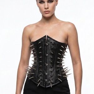 May include: A black strapless corset featuring a vertical front closure with silver-toned metal studs and rows of long, pointed silver spikes extending outwards from the sides and front panels, constructed with visible vertical seams.