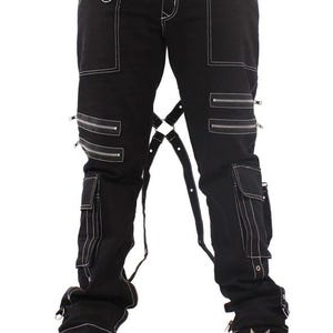 May include: Black pants with white stitching, multiple zippers, and cargo pockets. The pants feature straps and are paired with black platform boots with metal studs. The overall style is edgy and alternative.