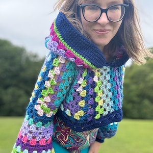 May include: A colorful, crocheted hooded sweater. The sweater features a granny square design with a mix of blue, purple, green, pink, and yellow yarn. The hood and cuffs are a solid dark blue. The sleeves are long and the sweater is cropped.