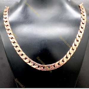 Puede incluir: Un collar de cadena de oro rosa con un diseño de eslabones de acera. El collar se exhibe en un maniquí negro, mostrando el metal pulido y los eslabones planos e interconectados de la cadena. El collar es una pieza llamativa.