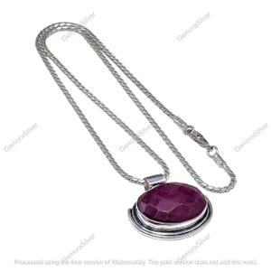 May include: A silver necklace with a large, faceted, oval-shaped, deep red pendant. The pendant is set in a silver bezel with a decorative swirl design. The chain is a fine, linked style with a lobster clasp.