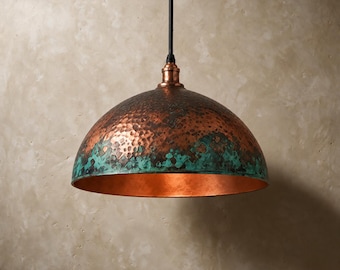 May include: A dome-shaped pendant light fixture featuring a hammered copper exterior with a prominent teal-colored patina finish along the lower edge. The interior of the metal shade is smooth and polished copper, suspended by a black cord.