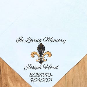 May include: A white handkerchief with the text "In Loving Memory" and the name "Joseph Horil" below a fleur-de-lis emblem. The dates 8/28/1910-9/24/2021 are also printed on the handkerchief.