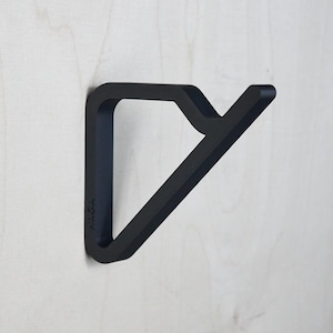 May include: A matte black wall hook with a geometric design. The hook is mounted on a light-colored wooden surface. The word "KASA" is printed on the side of the hook.