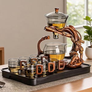 May include: A tea set featuring a dark glass teapot and six matching small cups with wooden handles, arranged on a black rectangular tray. A bronze-colored sculptural stand depicts a figure supporting the upper glass brewing vessel.