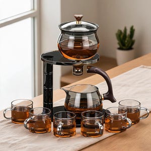Puede incluir: Un juego de té de cristal con un soporte negro de dos niveles, un recipiente superior con tapa y una tetera inferior con asa marrón oscuro. Seis tazas pequeñas de cristal llenas de té ámbar están dispuestas en semicírculo alrededor.