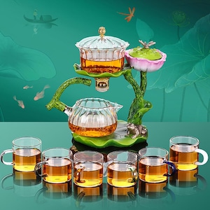 Puede incluir: Un juego de té de vidrio con un diseño decorativo de flor de loto. El juego incluye una tetera, un infusor de té y seis tazas de té de vidrio. El té es de color ámbar.