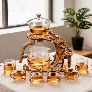 May include: A glass tea set featuring a clear teapot and six matching glass cups filled with amber liquid. The set is supported by a brown, wave-shaped stand with a small monk figurine. The teapot sits below a glass infuser with a lid.