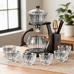 Peut inclure: Un service à thé en verre composé d'une théière cannelée avec une poignée en bois foncé, d'un infuseur assorti avec couvercle et de six petites tasses en verre cannelé. L'ensemble repose sur un support en bois foncé avec un porte-ustensiles.