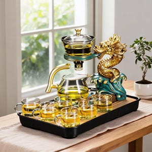 May include: A tea set featuring a clear glass teapot with a gold handle and six matching glass cups on a black tray. A gold and teal dragon sculpture supports a glass tea infuser above the teapot, all filled with golden tea liquid.