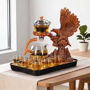 Peut inclure: Un service à thé composé d'une théière en verre et de six petites tasses en verre sur un plateau noir. Une sculpture en résine brune représentant un aigle perché sur un rocher soutient un infuseur à thé en verre au-dessus de la théière.