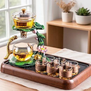 Peut inclure: Un service à thé composé d'une théière en verre et d'un infuseur sur un support en forme de lotus vert avec une anse dragon dorée. L'ensemble comprend six petites tasses en verre avec des manchons en bois, sur un plateau de service en bois.