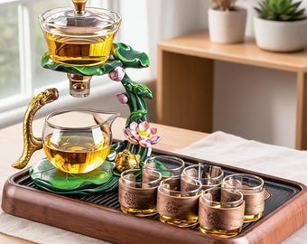 Könnte beinhalten: Ein Teeservice mit einer Glasteekanne und einem Glas-Teezubereiter auf einem grünen, lotusförmigen Ständer mit goldenem Drachengriff. Das Set enthält sechs kleine Glastassen mit Holzmanschetten auf einem rechteckigen Holztablett.