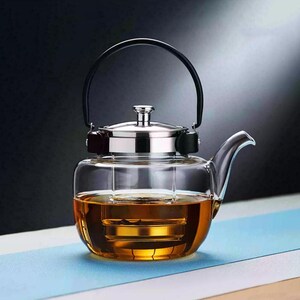 May include: A clear glass teapot with a stainless steel lid and a black handle. The teapot is filled with amber-colored liquid, likely tea, and has a built-in infuser. The design is modern and minimalist, suitable for brewing tea.