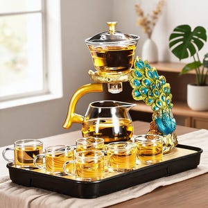 Puede incluir: Un juego de té de cristal con una tetera transparente y seis tazas pequeñas llenas de té ámbar. El conjunto incluye un soporte dorado con una figura de pavo real decorada en azul y verde, todo dispuesto sobre una bandeja rectangular negra.