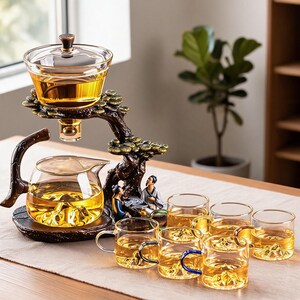 Peut inclure: Un service à thé en verre composé d'une théière transparente et d'un infuseur supérieur soutenu par un support en forme d'arbre brun foncé avec deux petites figurines. Six tasses en verre avec anses, contenant un liquide doré et une base en relief.