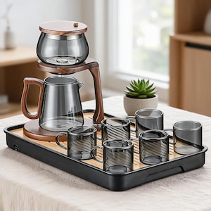 Op de afbeelding: Een theeset bestaande uit een donkergrijze glazen theepot met een houten deksel en handvat, een bijpassende glazen infuser en zes kleine grijze glazen mokken met een geribbelde textuur, geplaatst op een rechthoekig zwart dienblad met houtinleg.