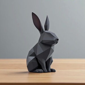 May include: A geometric, dark gray rabbit figurine with a polygonal design. The rabbit is seated, with its ears upright and a red nose. The figurine is placed on a wooden surface against a gray background. This decorative item could be used as a home decor accent.