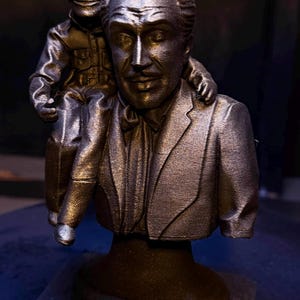 Peut inclure: Buste en bronze représentant deux personnages, l'un assis sur les épaules de l'autre. La sculpture est montée sur un socle rectangulaire avec l'inscription "Professor Vutible".