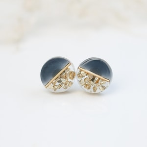 May include: A pair of round stud earrings with a clear resin base and a gold fleck design. The top half of each earring is a dark grey colour.